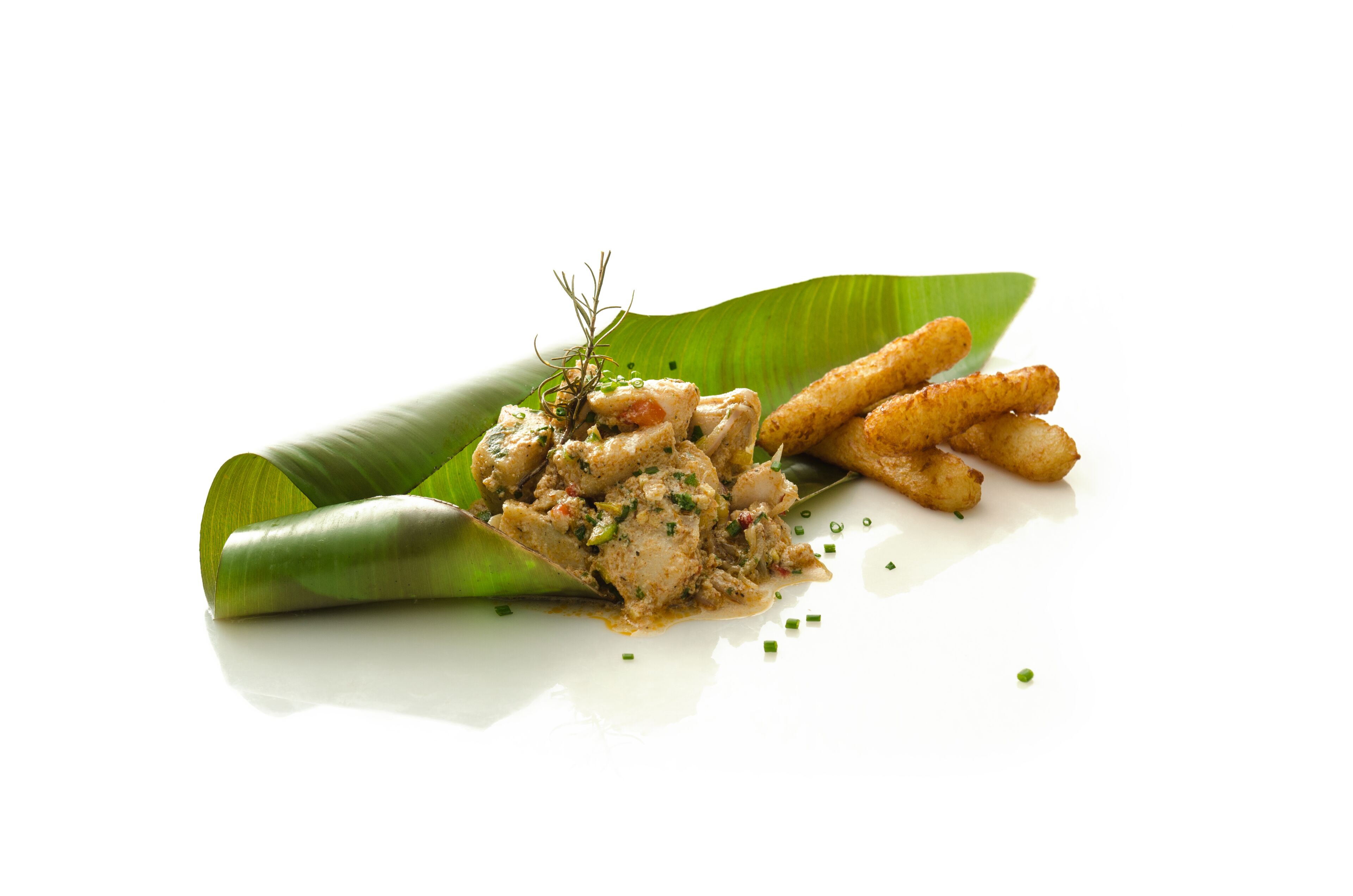 A dish of chicken and fries on a banana leaf with garnish.