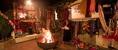 A traditional market with a fire pit in the center, surrounded by various textiles and bags.