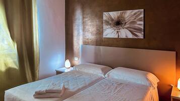 Una habitación de hotel con dos camas, un cuadro de flores en la pared y una mesita de noche con una lámpara.