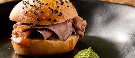 Un sándwich con un palillo, salsa verde y un plato oscuro.