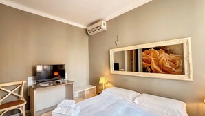A hotel room with a bed, a desk with a TV, a chair, a lamp, and a wall-mounted mirror. - Hotel Alba (Lavagna)