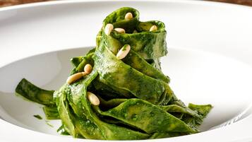 Un piatto di pasta verde con pignoli su un piatto bianco.