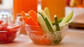 Una encimera de cocina con un bol de verduras cortadas, un vaso de zumo de naranja y una botella de zumo de naranja.