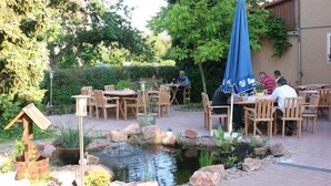 An outdoor patio with wooden tables and chairs, a small pond, and potted plants.