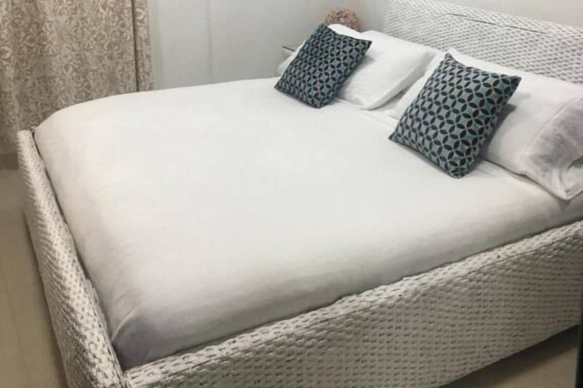 A neatly made bed with patterned pillows, a round mirror, and an air conditioning unit on the wall.