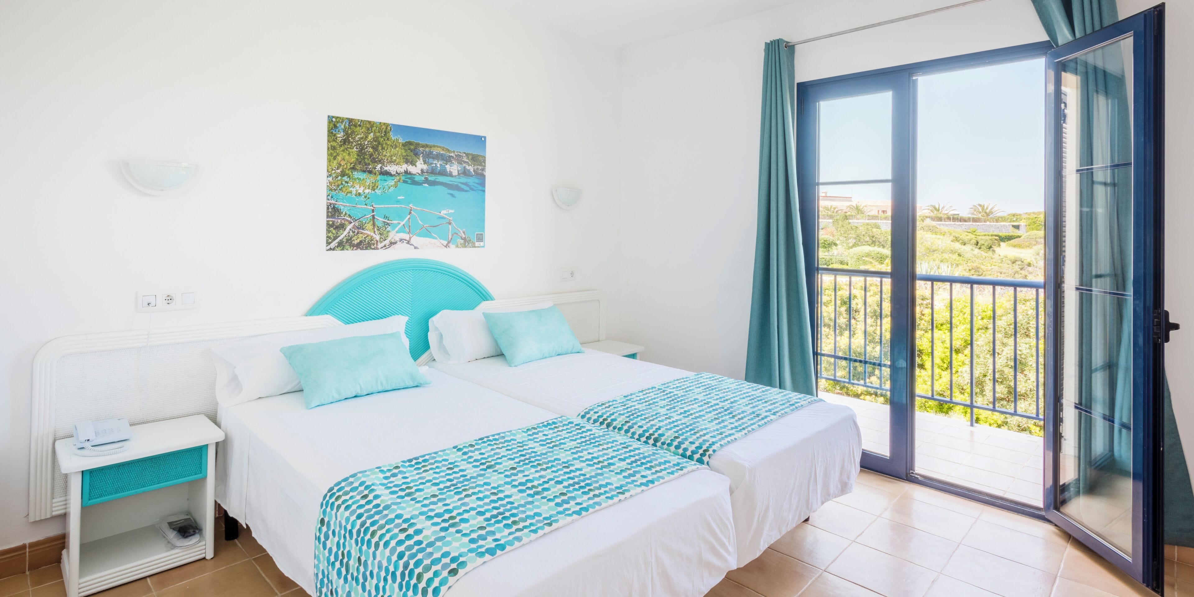 A hotel room with a bed, a nightstand, a window with a view, and a door to an outdoor balcony.