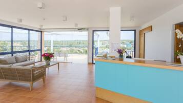 A spacious reception area with a blue counter, a wicker sofa, a wooden bench, and a view of the city through large windows.