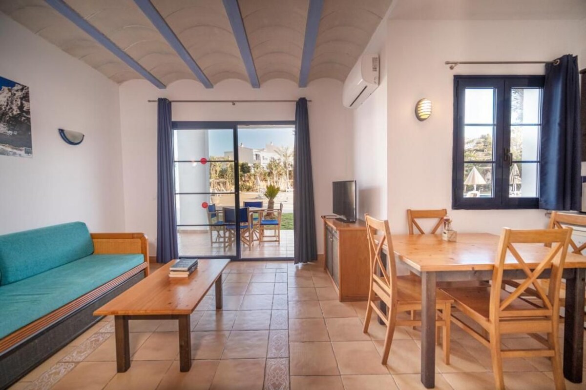 Una sala de estar con sofá, mesa de centro, televisor y comedor con sillas y mesa.