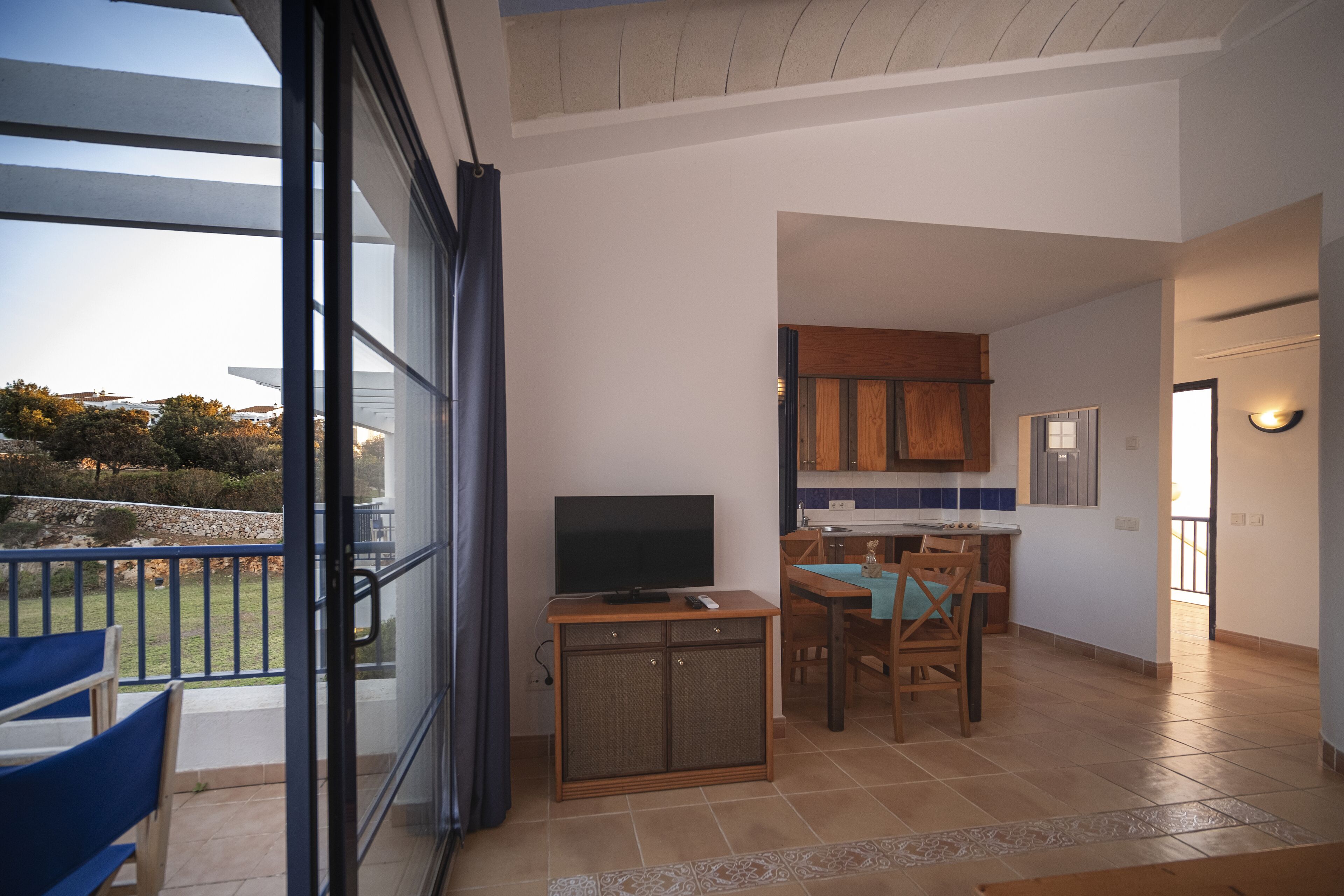 A spacious living area with a balcony, a kitchen with wooden cabinets, and a dining area with a table and chairs.