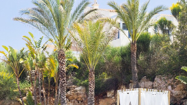 A clear blue pool with a wooden deck and a white canopy bed. -  Bimbolla Apartaments (Sant Lluis)