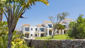 A multi-story building with a stone retaining wall, surrounded by greenery and palm trees. -  Bimbolla Apartaments (Sant Lluis)