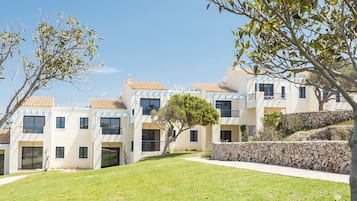 Une rangée d’immeubles modernes à plusieurs étages, dotés de balcons, avec un mur de soutènement en pierre et une pelouse à l’avant.