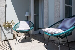 Dos sillas de mimbre con cojines a rayas, una mesita y una planta en maceta sobre un patio de concreto.