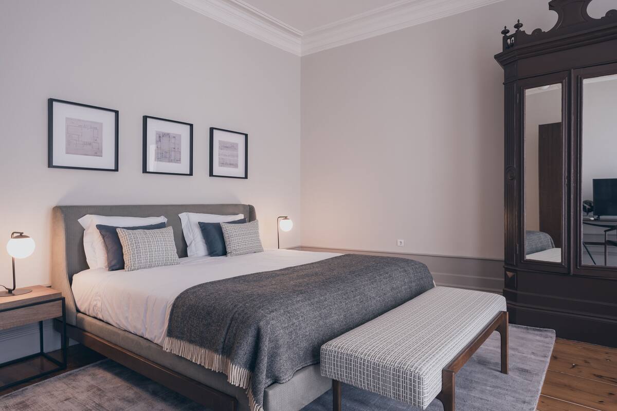 A neatly arranged bedroom with a bed, bedside tables, a bench, and framed architectural drawings on the wall.