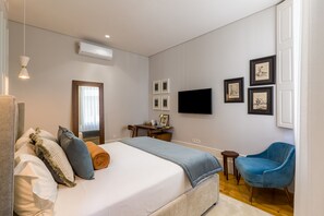 Un dormitorio con cama, mesita de noche, silla y televisor montado en la pared.
