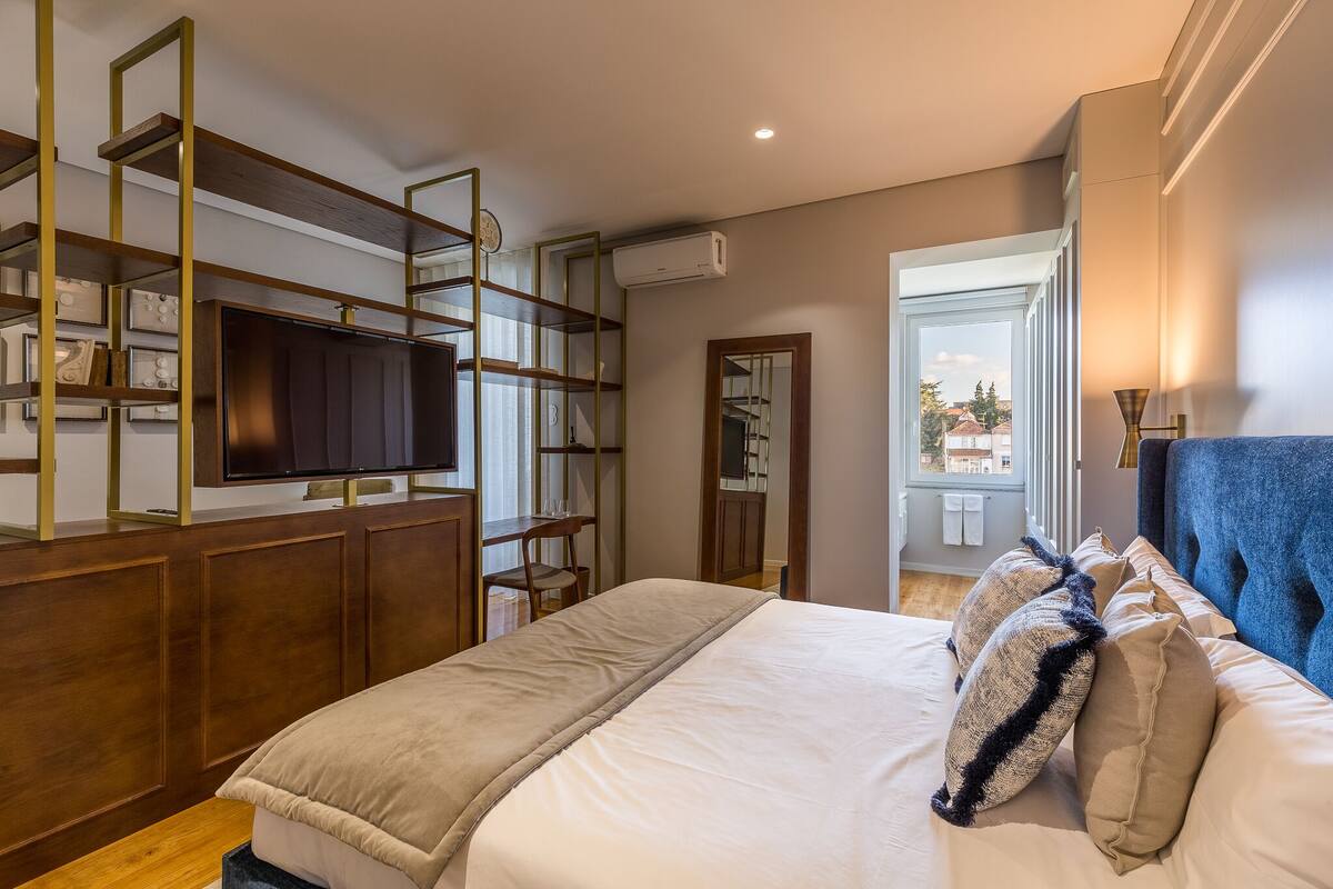 A bedroom with a bed, a TV, a wooden wardrobe, and a balcony view.