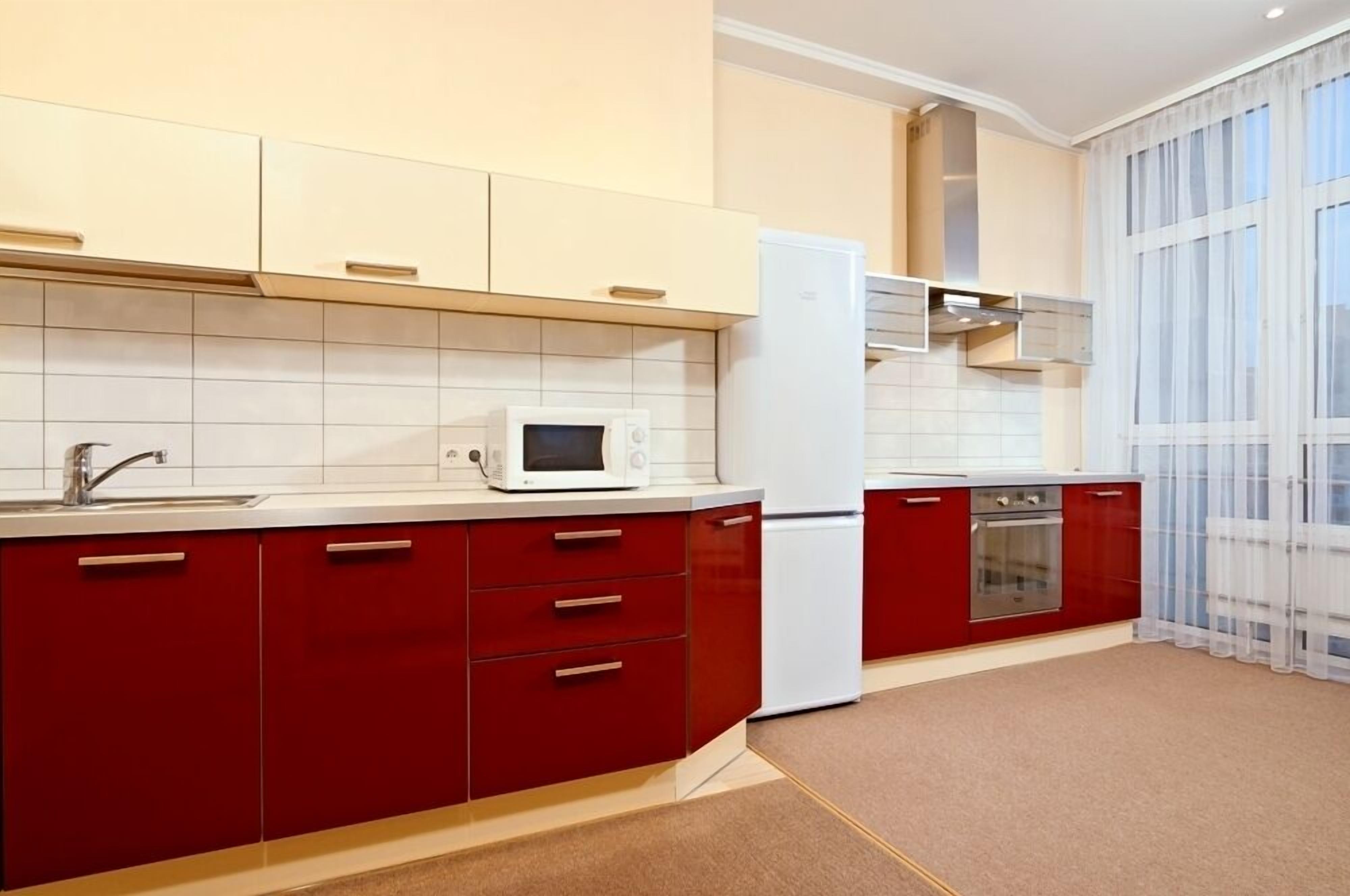 A modern kitchen with red cabinets, a white refrigerator, a microwave, and a built-in oven.