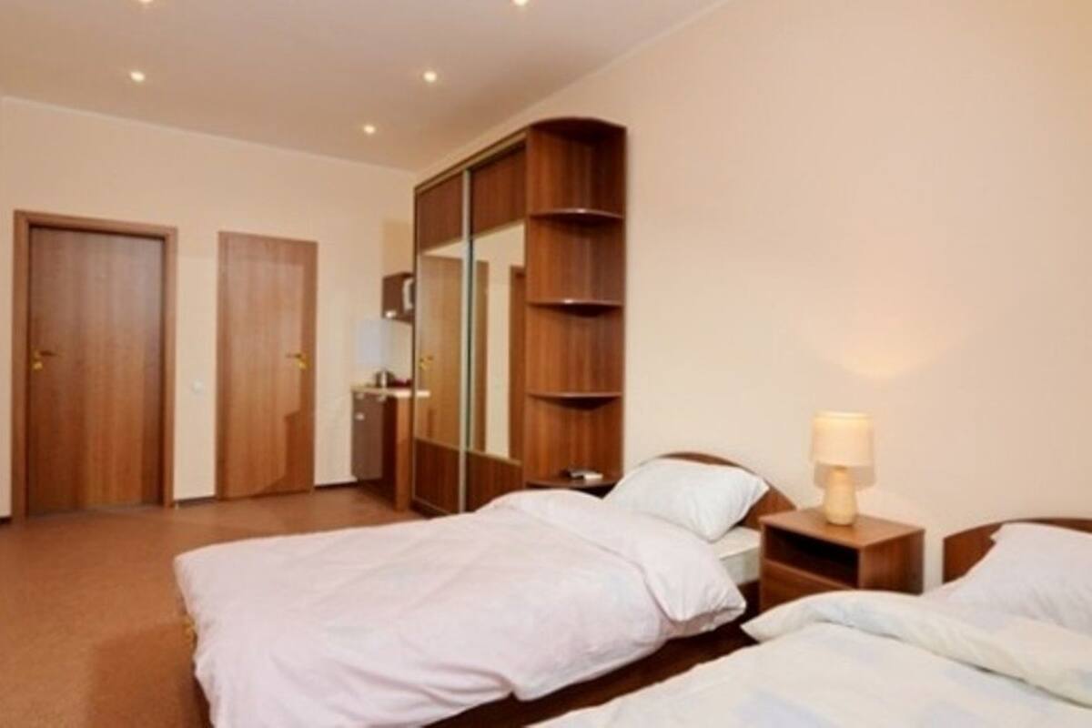A hotel room with two beds, a wardrobe, a mirror, and a bedside table with a lamp.