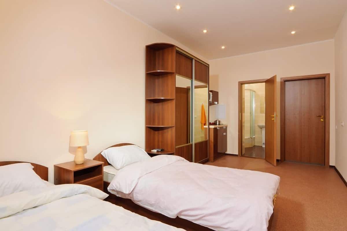 A hotel room with two beds, a wardrobe, a mirror, and a bathroom door.