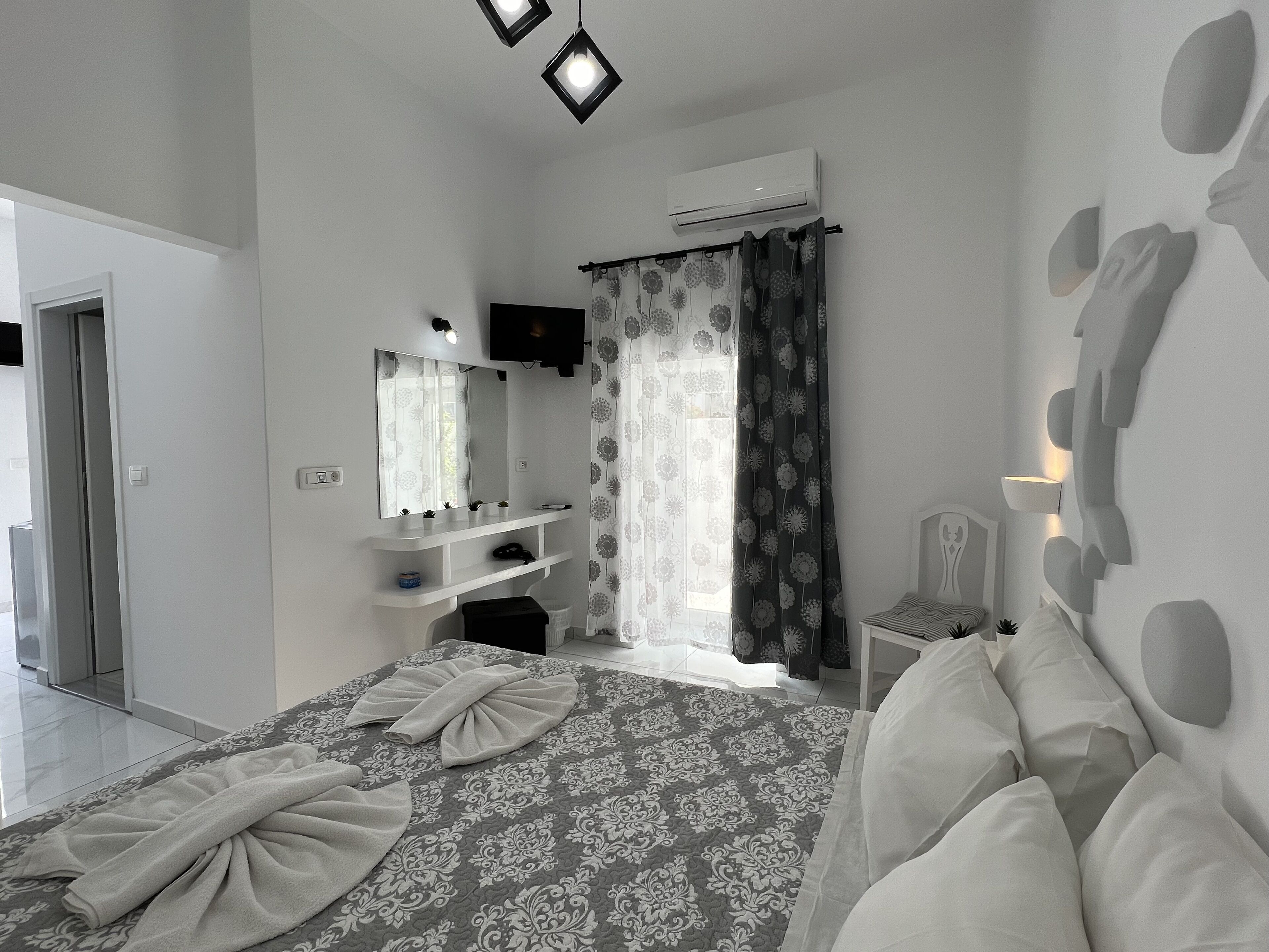 A modern bedroom with a large bed, a bedside table, a mirror, a wardrobe, and an air conditioning unit.