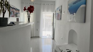 A bright hallway with a white floor, a hanging pendant light, a vase with red flowers, and a door leading to another room. - Villa Pavlina (Santorini)