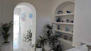 A hallway with white walls, potted plants, and shelves with decorative items. - Villa Pavlina (Santorini)