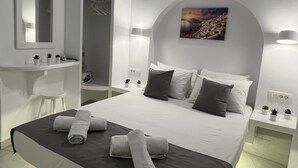 A modern hotel room with a bed, a bedside table, a mirror, a painting, and a small plant on the nightstand. - Villa Pavlina (Santorini)