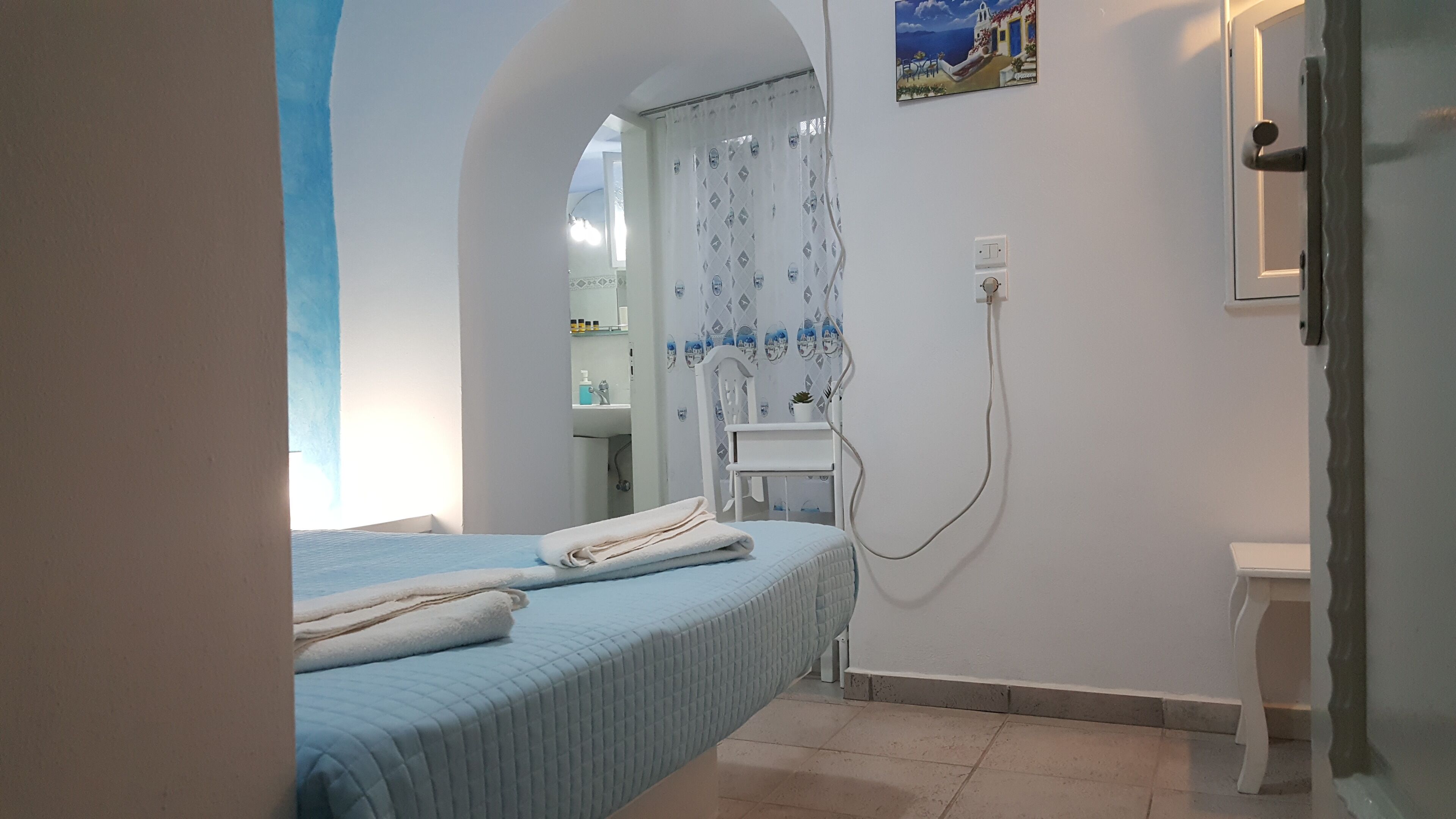 Un dormitorio con cama, mesita de noche, espejo y lámpara de pared.