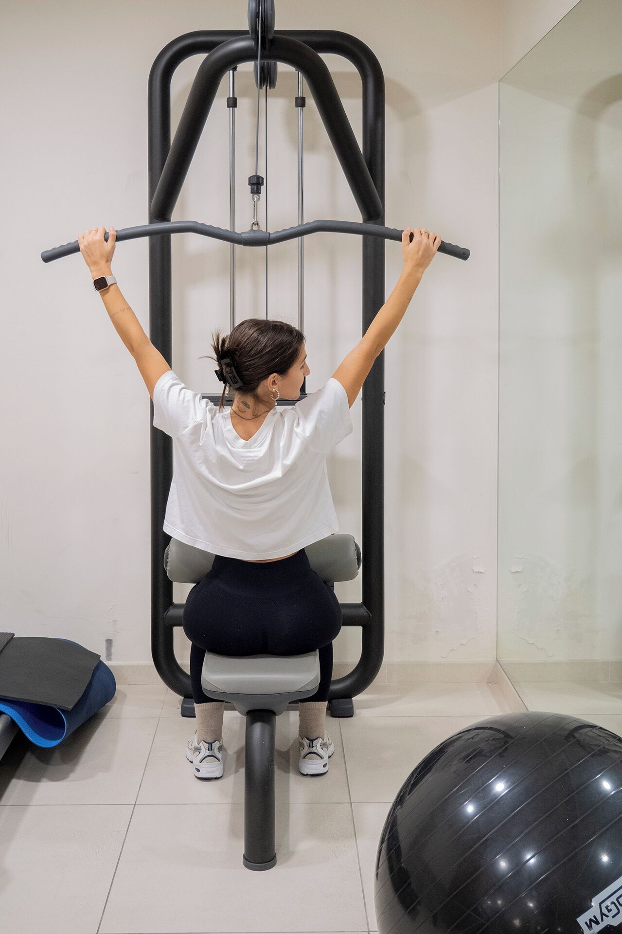 A person using a gym machine with a pull-up bar, seated on a grey bench.