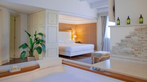 A hotel room with a bed, a nightstand, a plant, a bathroom with a bathtub, and a stone fireplace. - Villa Michelangelo (Citta Sant'Angelo)