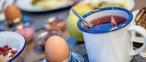 Una mesa con una taza azul que contiene líquido rojo, un soporte metálico para huevos con un huevo marrón, y varios platos al fondo.