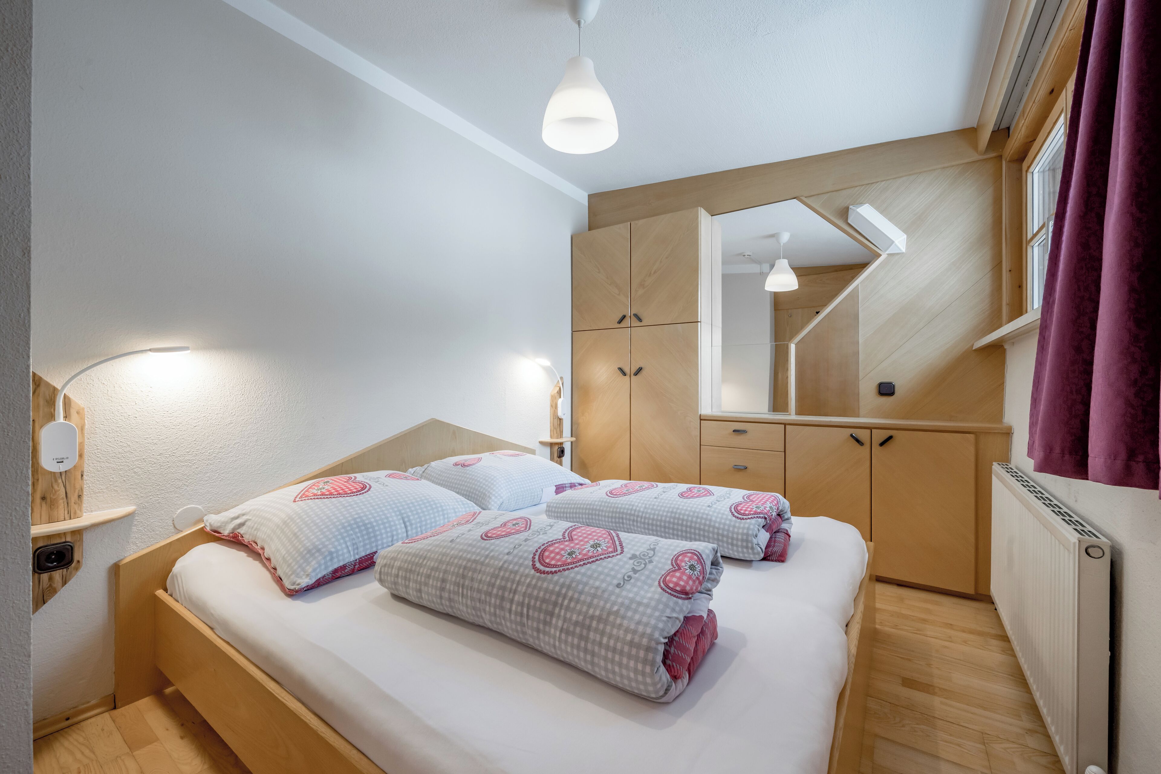 Ein Schlafzimmer mit Bett, Nachttischen, einem Kleiderschrank, einem Spiegel und einem Fenster mit Vorhängen.