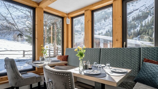 A cozy dining area with wooden beams, large windows, and a view of a snowy landscape. - Landhaus Edelweiss (Sankt Leonhard im Pitztal)