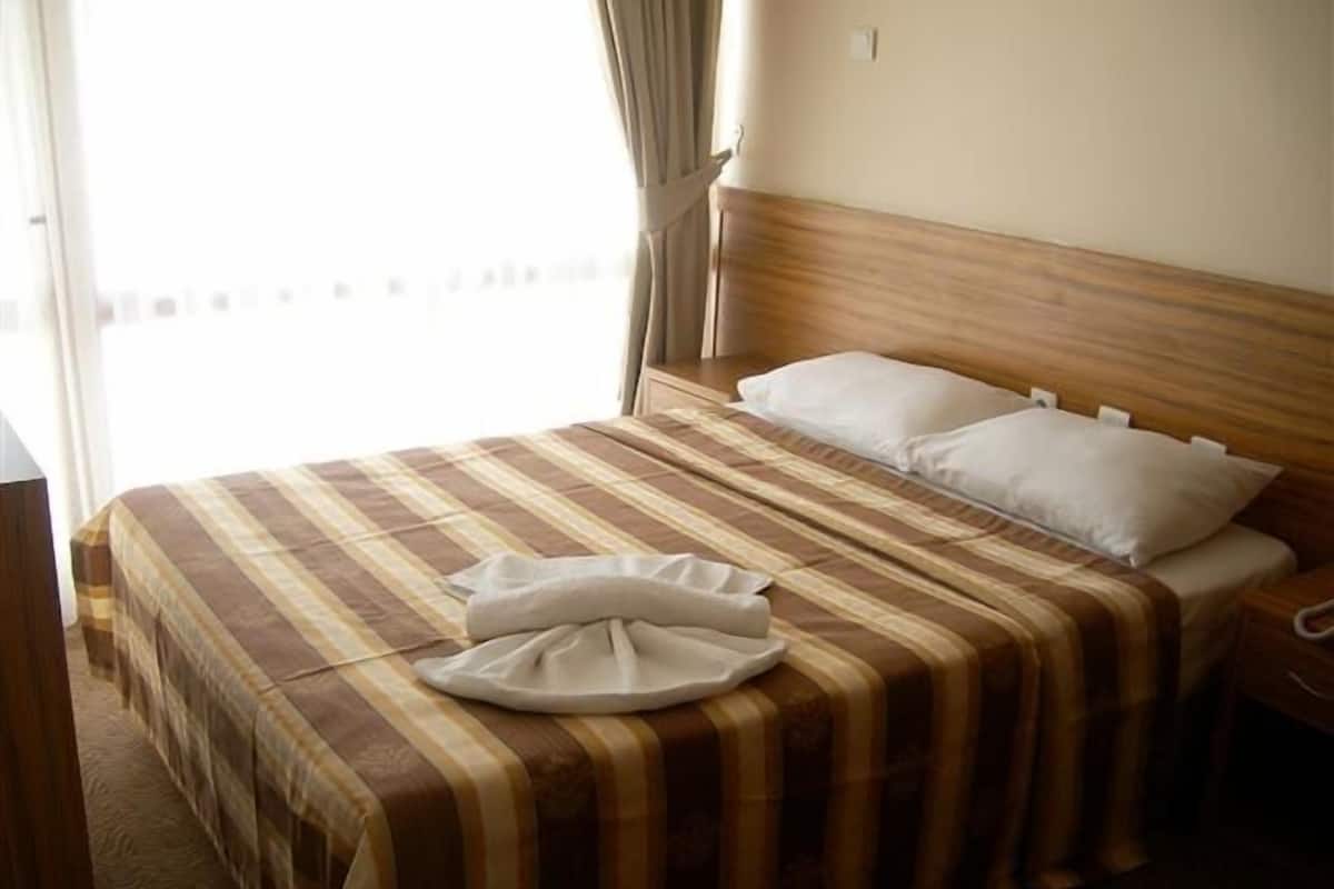 A hotel room with a bed, a bedside table, and a window with curtains.