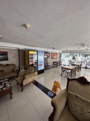 A hotel lobby with sofas, a refrigerator, a coffee table, and a dining area with tables and chairs. - Lara Kapris Hotel (Antalya)