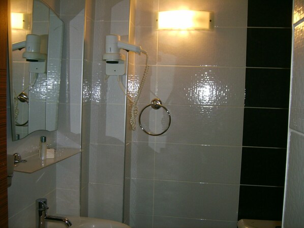 A bathroom with a mirror, a sink, a toilet, and a shower with a towel ring.