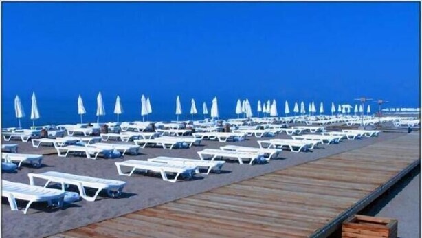 Una playa con filas de sillas blancas y sombrillas, un paseo marítimo de madera y un cielo azul despejado.