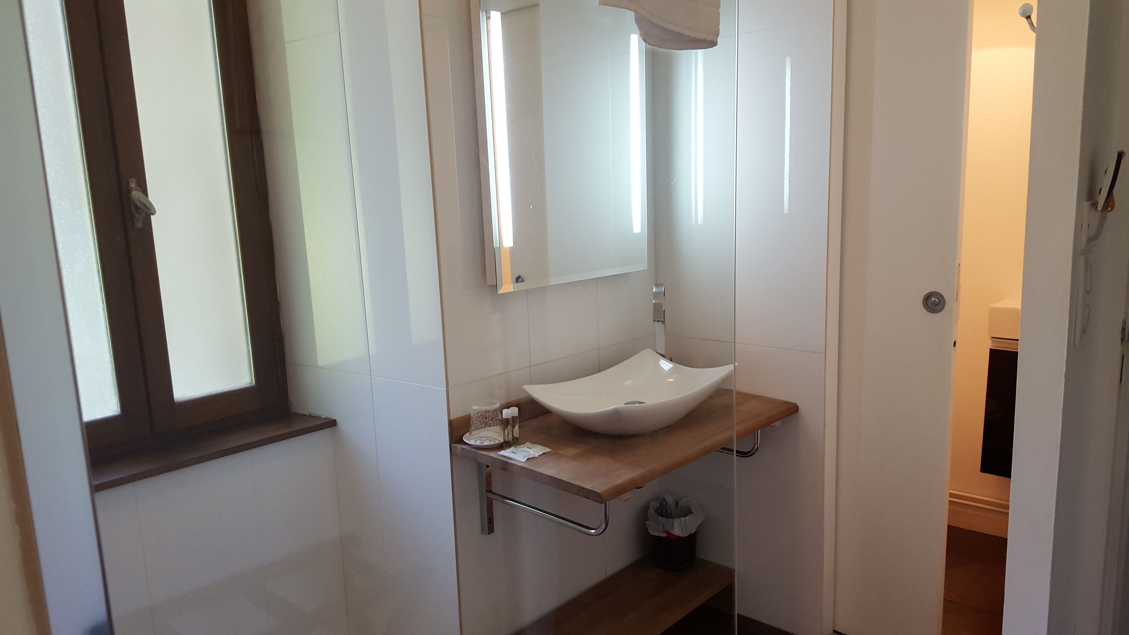 A modern bathroom with a white sink, a mirror, and a window.