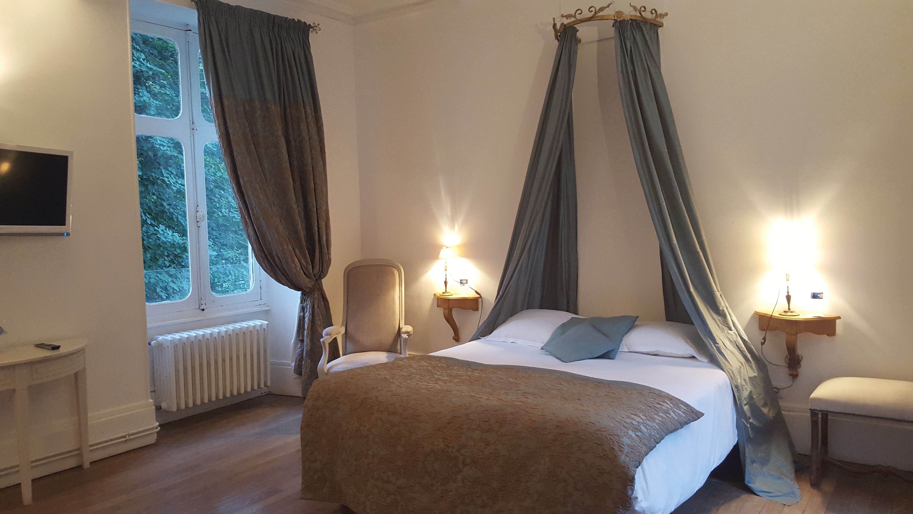 Een slaapkamer met een bed, twee bedlampen, een stoel, een televisie en een raam met gordijnen.