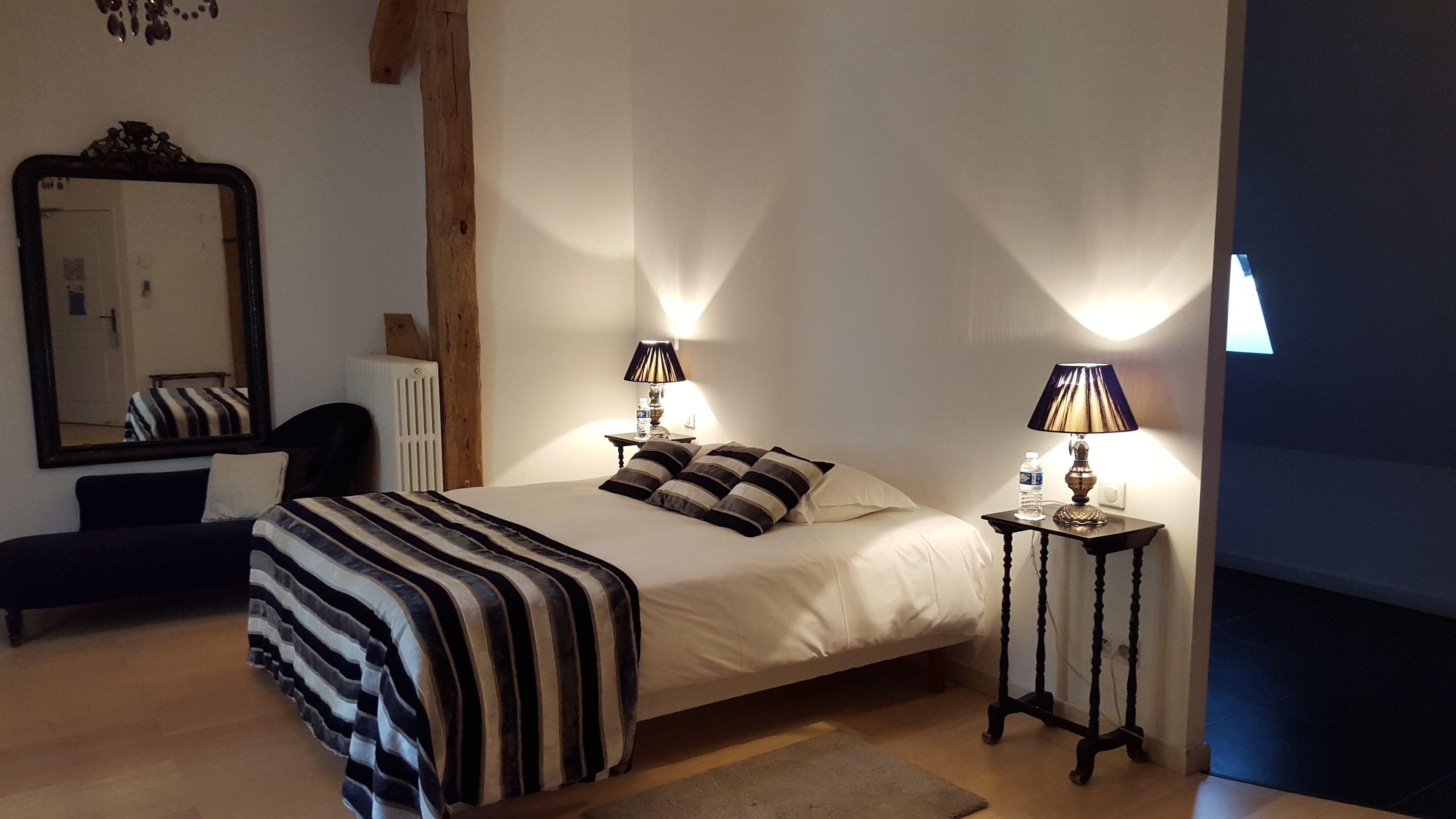 Une chambre à coucher avec un lit, deux tables de chevet avec des lampes, un grand miroir et un radiateur.