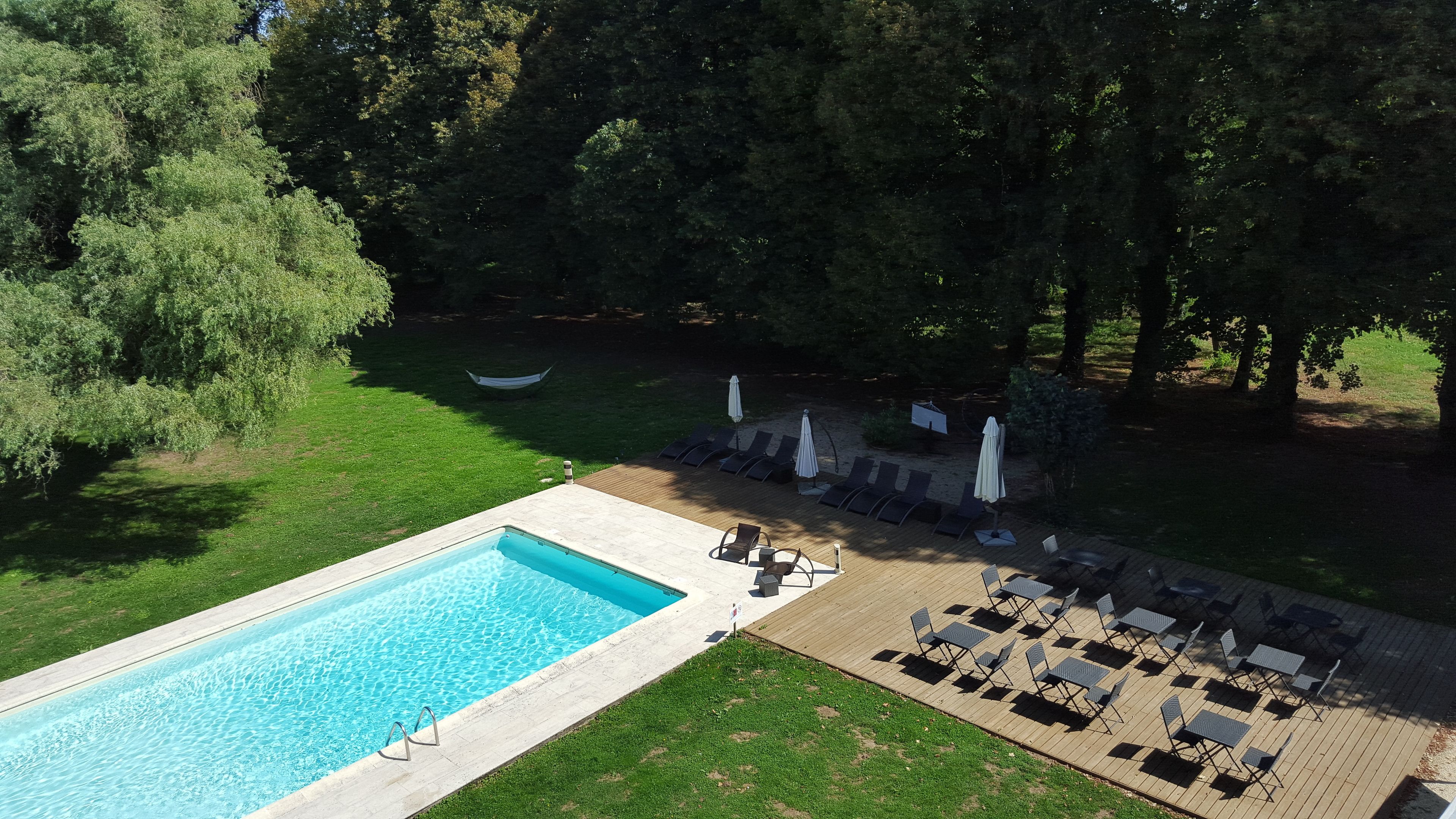 A rectangular swimming pool with a wooden deck, surrounded by lounge chairs and umbrellas.