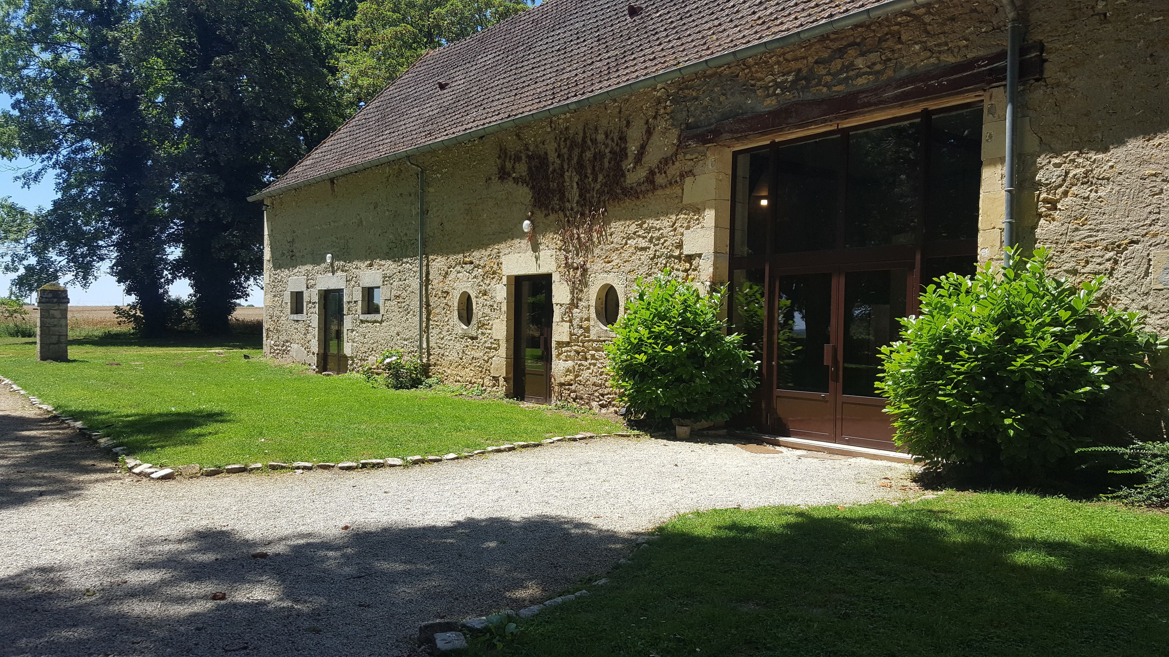 A rustic stone building with a gravel driveway, a wooden door, and a large window.