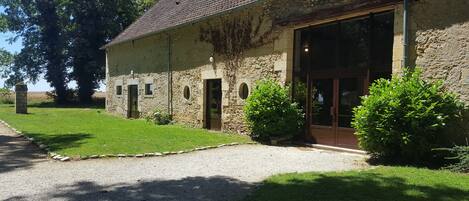 A rustic stone building with a gravel driveway, a wooden door, and a large window.