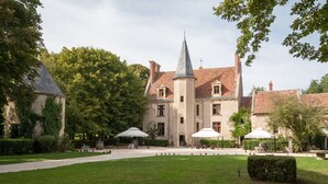 Un edificio histórico con una torre, rodeado por un jardín bien cuidado con mesas al aire libre.