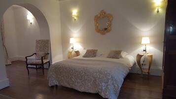 A bedroom with a large bed, two nightstands with lamps, a chair, and a decorative mirror on the wall.