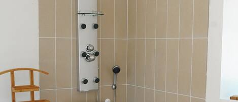 A bathroom with a shower, a towel rack, a small table with toiletries, and a wooden drying rack.