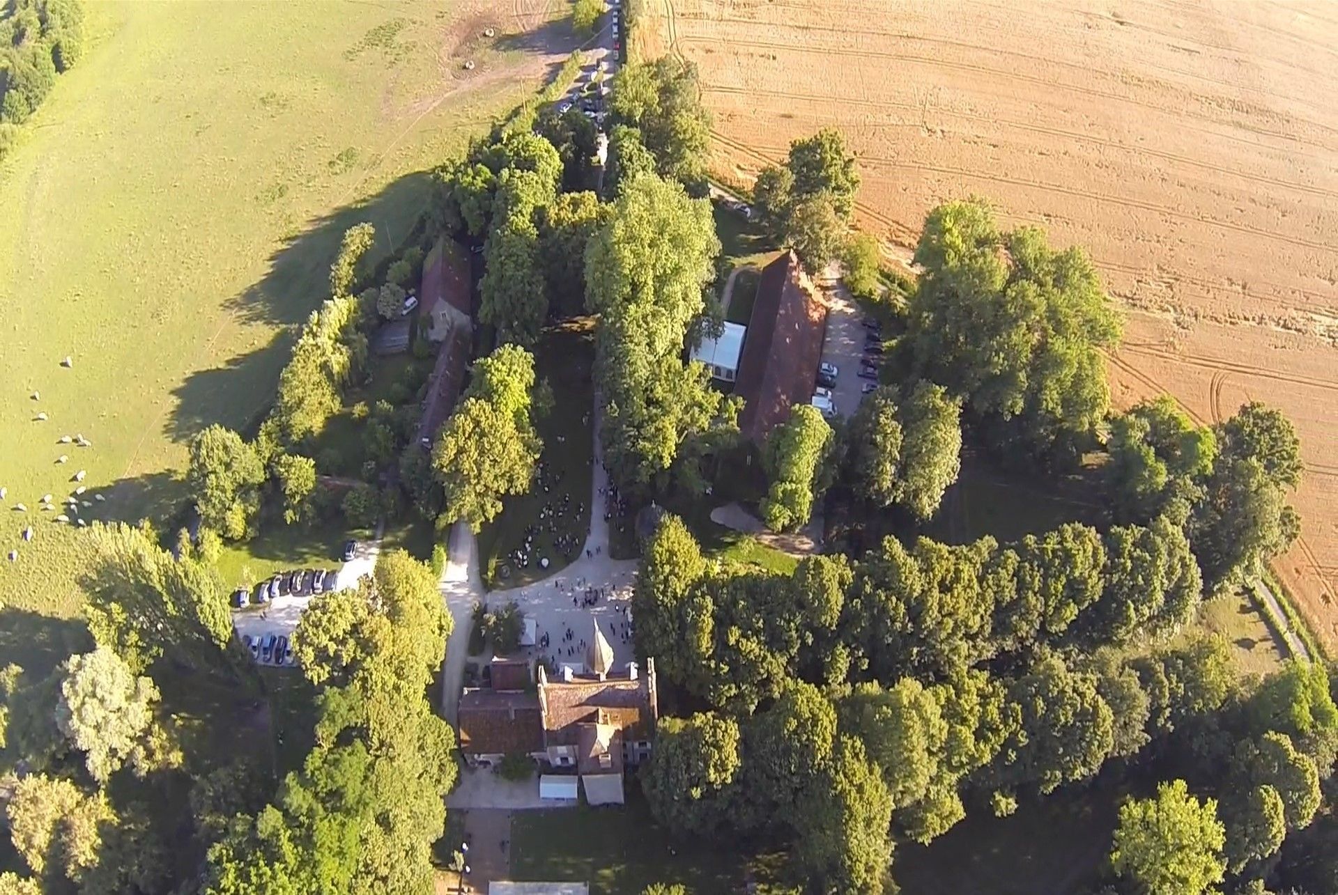 Vista aérea de una propiedad con un edificio central rodeado de árboles, un área de estacionamiento y campos abiertos.