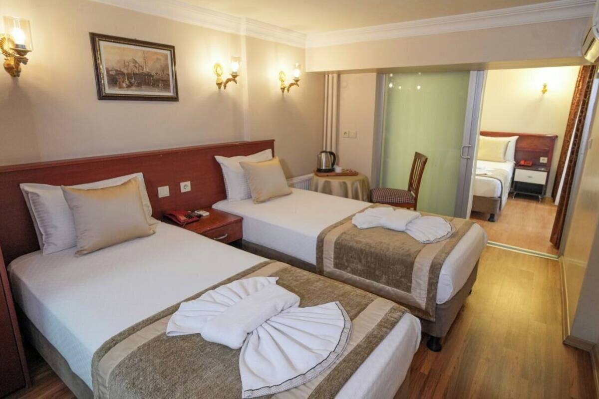 A hotel room with two beds, a small table with a lamp, a chair, and a mirror.