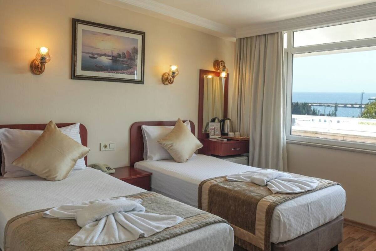 A hotel room with two beds, a large window with a view, a painting on the wall, and a mirror.