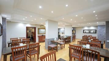 Un comedor amplio con varias mesas y sillas de madera, una isla central con fregadero, y una cocina al fondo.